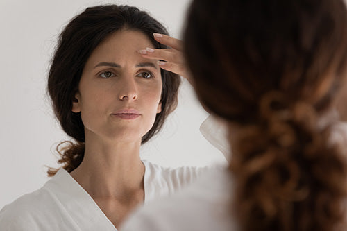 Woman looking in mirror touching forehead