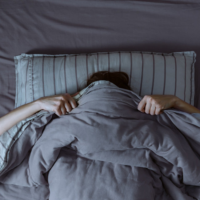 Top view of woman in bed covering her face with blanket.