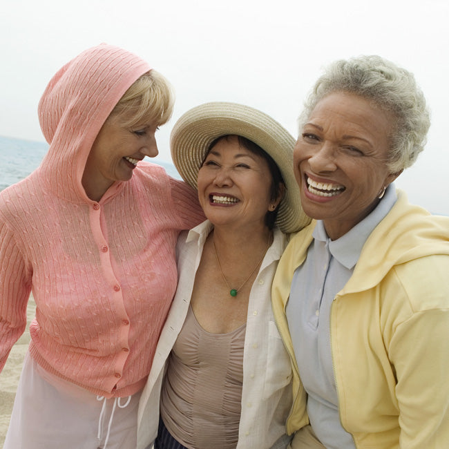 Three middle aged women smiling in an embrace on the beach