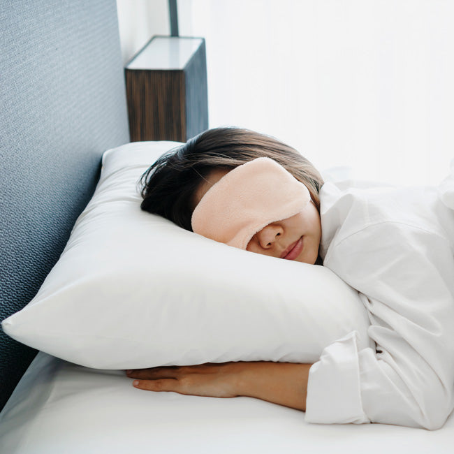 Closeup of woman in sleeping mask lying in comfortable white bed in the morning.