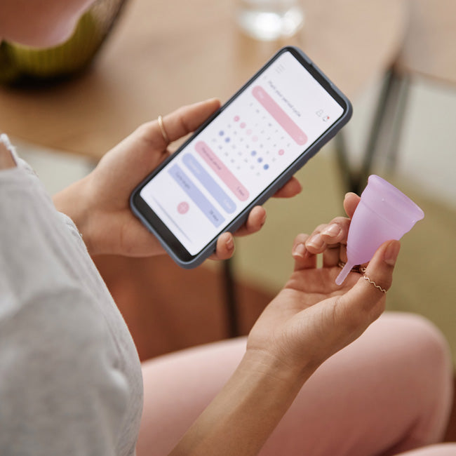 Closeup of woman holding menstrual cup and smartphone with period tracker app