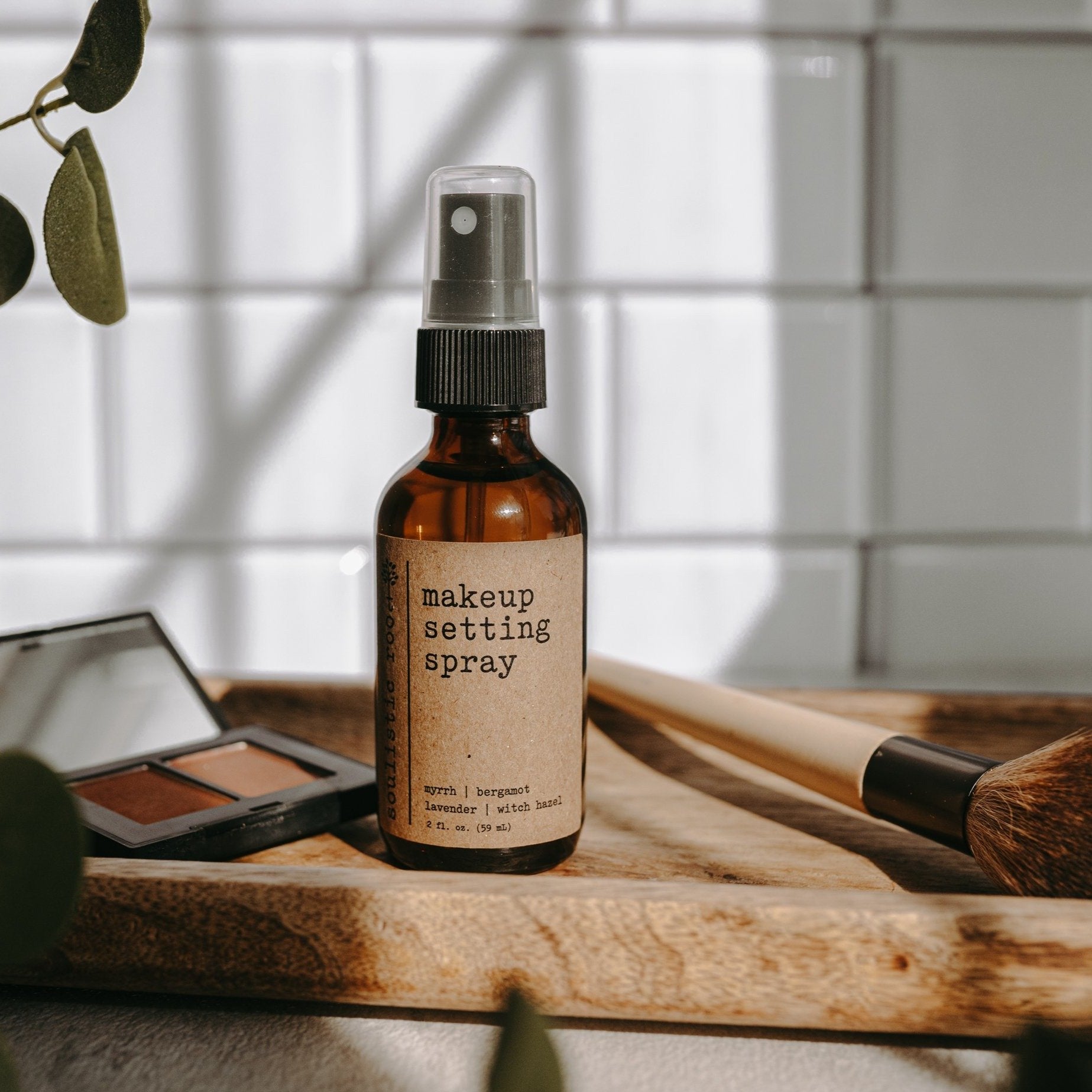 Small bottle of Soulistic Root Makeup Setting Spray in a bathroom tray with makeup and a makeup brush in the background