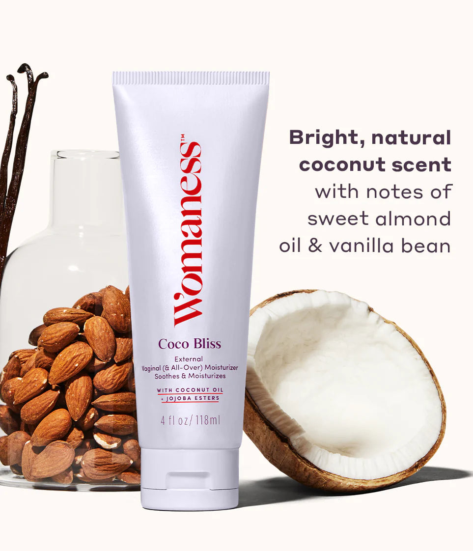 Image of Womaness Coco Bliss product with vanilla bean, almonds and coconut in the background. The copy over the image reads Bright, natural coconut scent with notes of sweet almond oil and vanilla bean