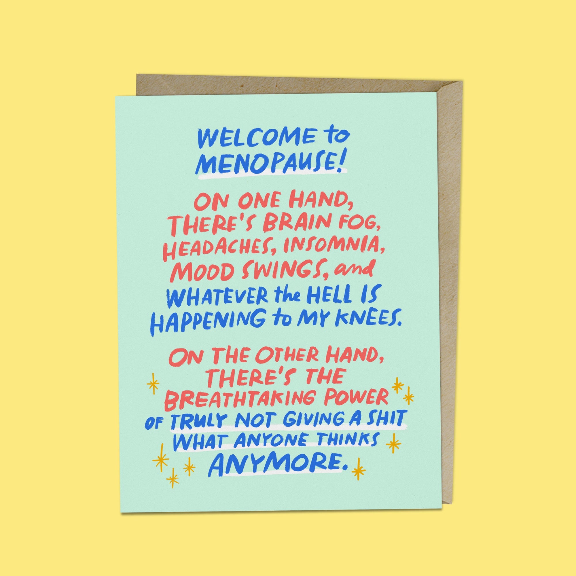 a flat greeting card on a colored background. The card has an envelope behind it. The Card reads: A person holding a small greeting card that reads: A greeting card that reads: "Welcome to menopause! On one hand, there’s brain fog, headaches, insomnia, mood swings, and whatever the hell is happening to my knees. On the other hand, there’s the breathtaking power of truly not giving a s*t what anyone thinks anymore." 